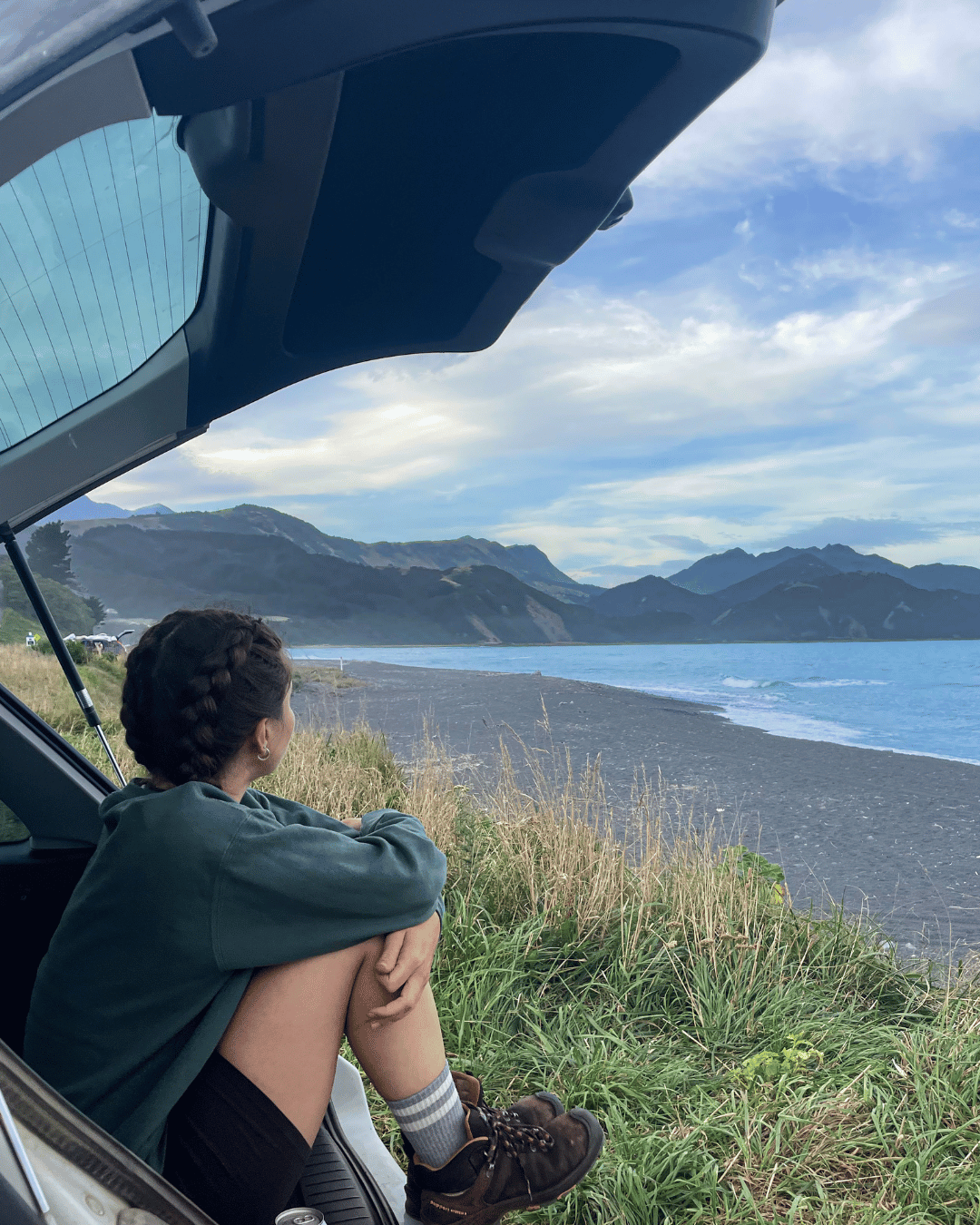 Clem sitting on a car roof looking out at a lake and mountain landscape