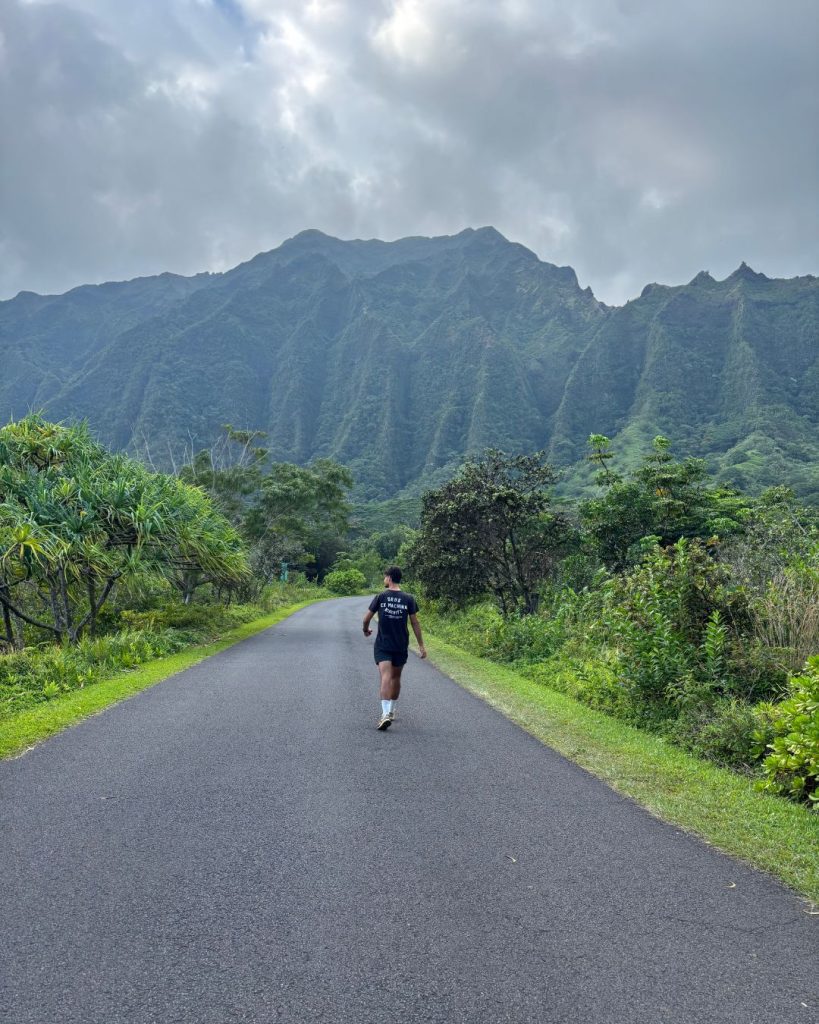 Person jogging along a paved path at Hoomaluhia Botanical Garden with the dramatic Koolau mountain ridge behind