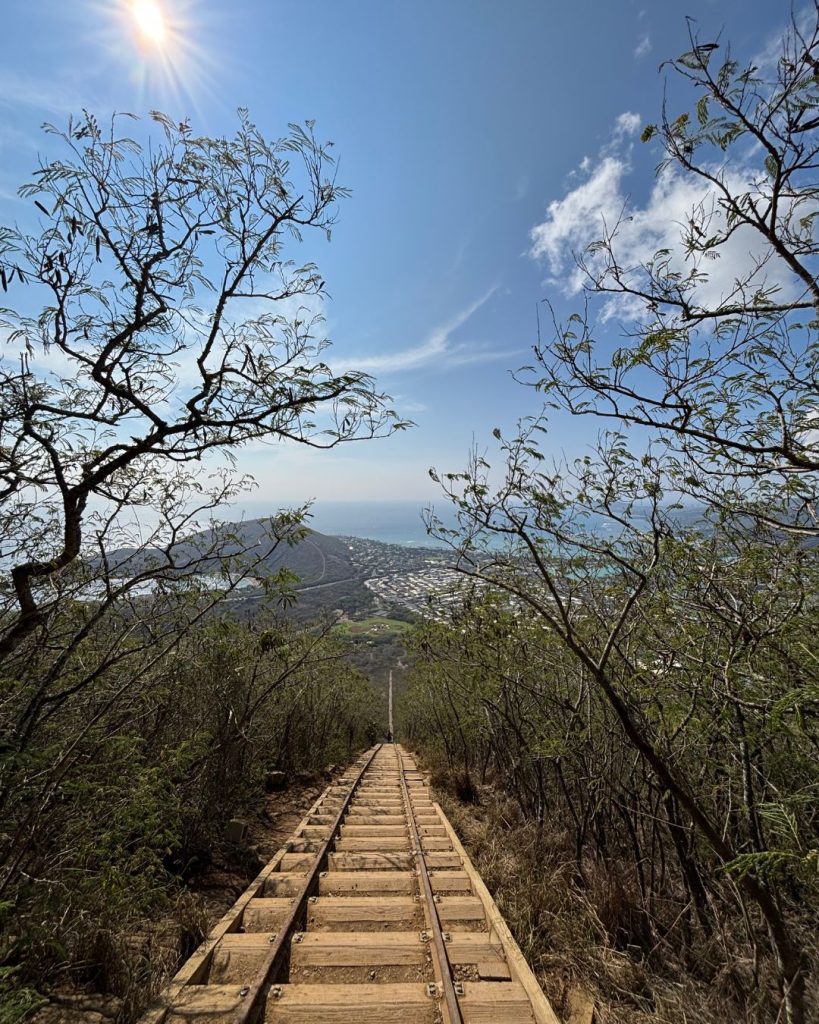 Steep old railway trestle steps climbing Koko Crater with sun flare and coastal view below