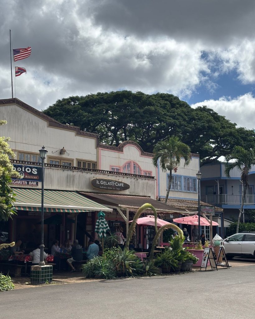 Historic storefronts with awnings and a shave ice shop along Haleiwa's main street under a cloudy sky