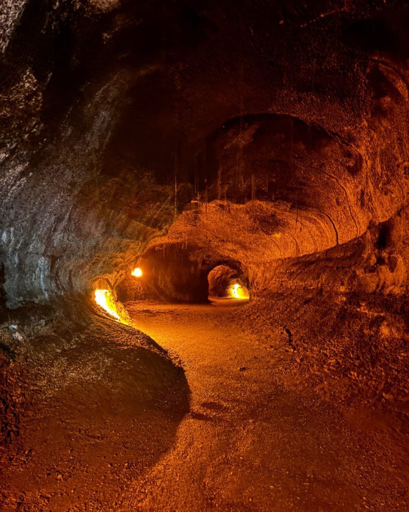 The inside of a lava tube lit orange, with two hikers silhouetted in the tunnel ahead