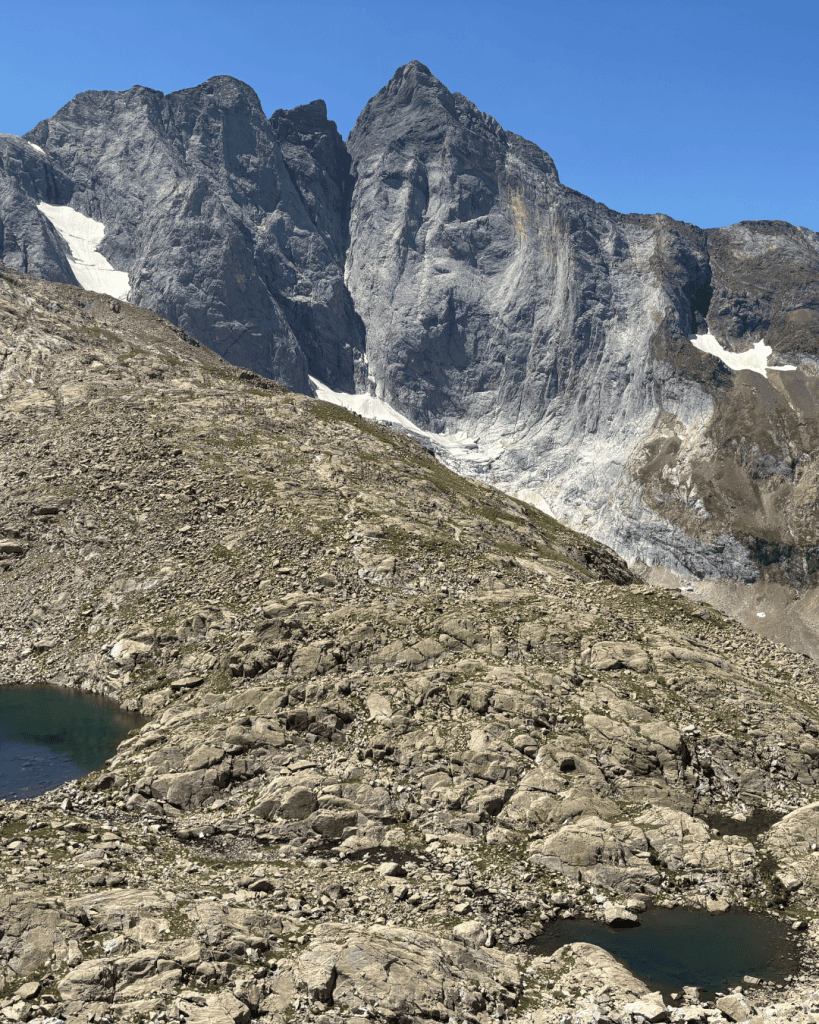 Rocky peak with patches of snow above small glacial pools near Col d'Arraillé