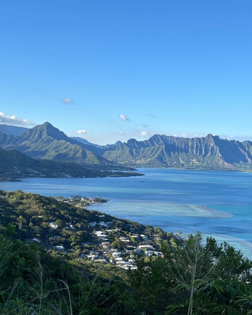 View of Kaneohe Bay's turquoise waters and coastal homes with green mountain ridges rising behind