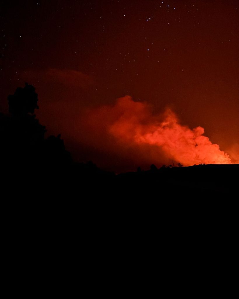 A red glow and a plume of steam rising from the volcano at night