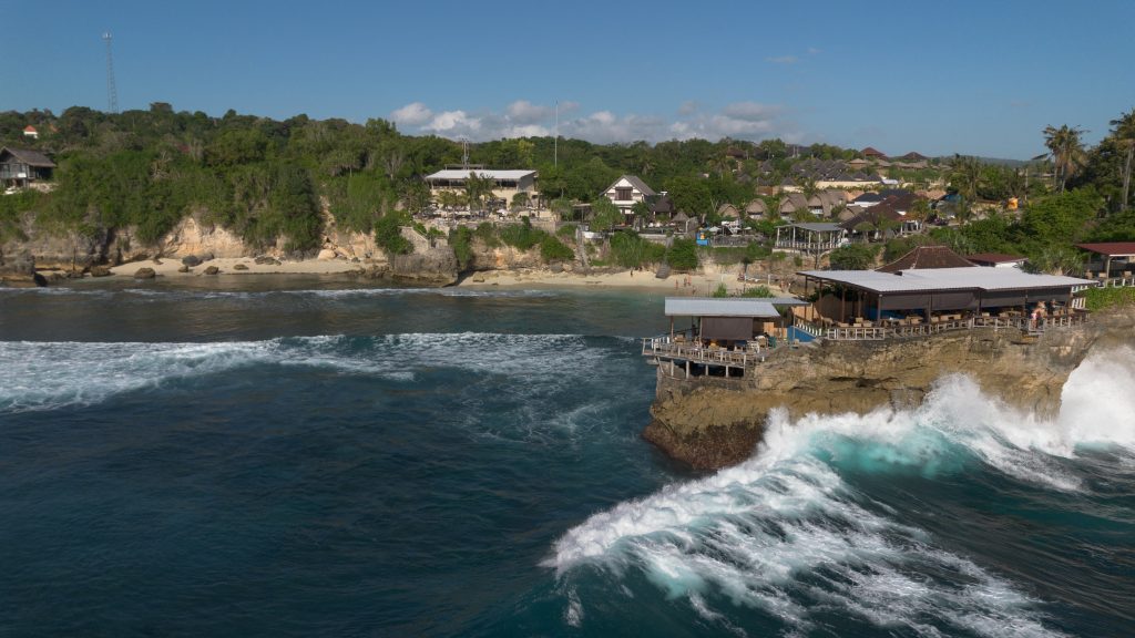 Aerial view of waves breaking along Nusa Lembongan's rugged coastline near the village