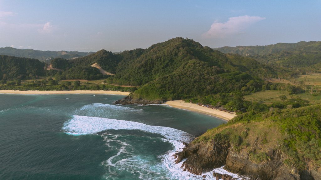 Aerial view of a curved white sand bay backed by green hills near Kuta Lombok