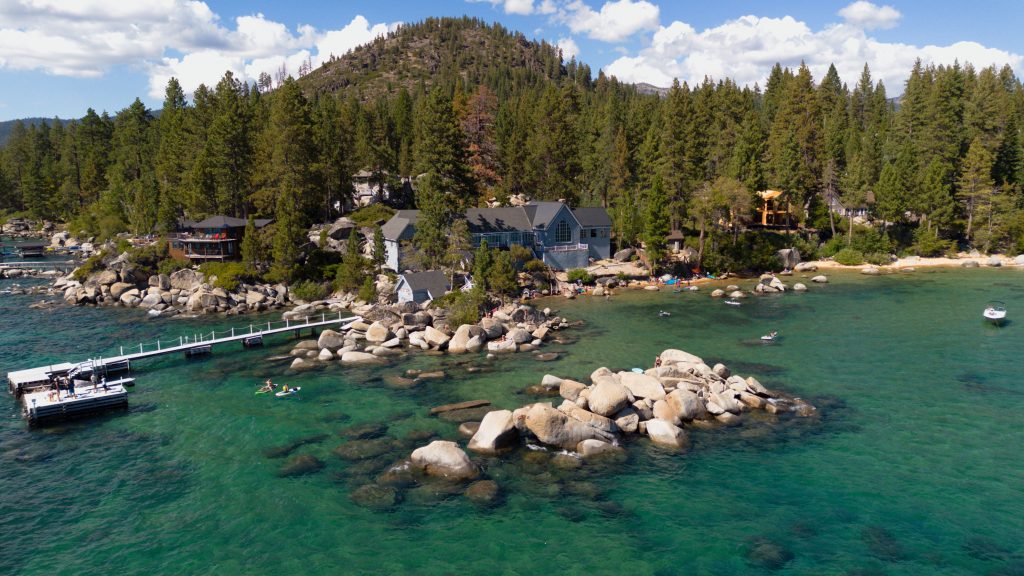 Aerial view of a forested lake shore with clear turquoise water, shot with the best drone for travel