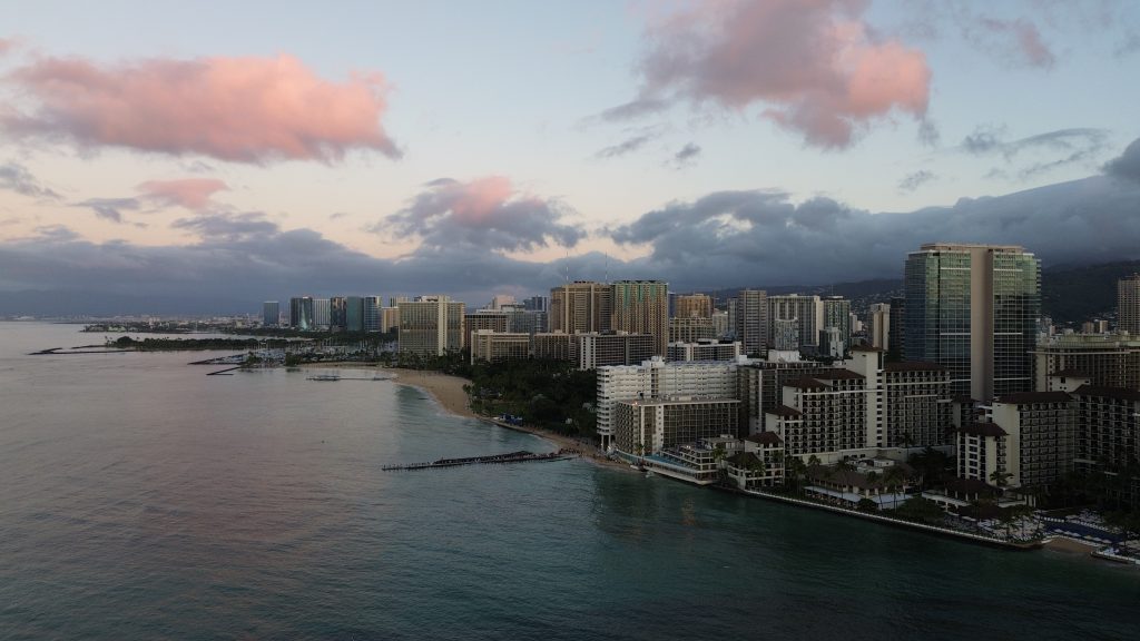 Aerial view of Waikiki's beach and hotel skyline at dusk with pink clouds overhead