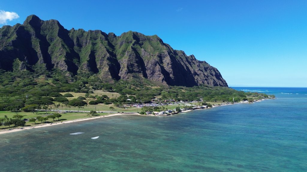 Aerial view of Kualoa Regional Park with the jagged Koolau mountains rising behind a coastal park and turquoise ocean