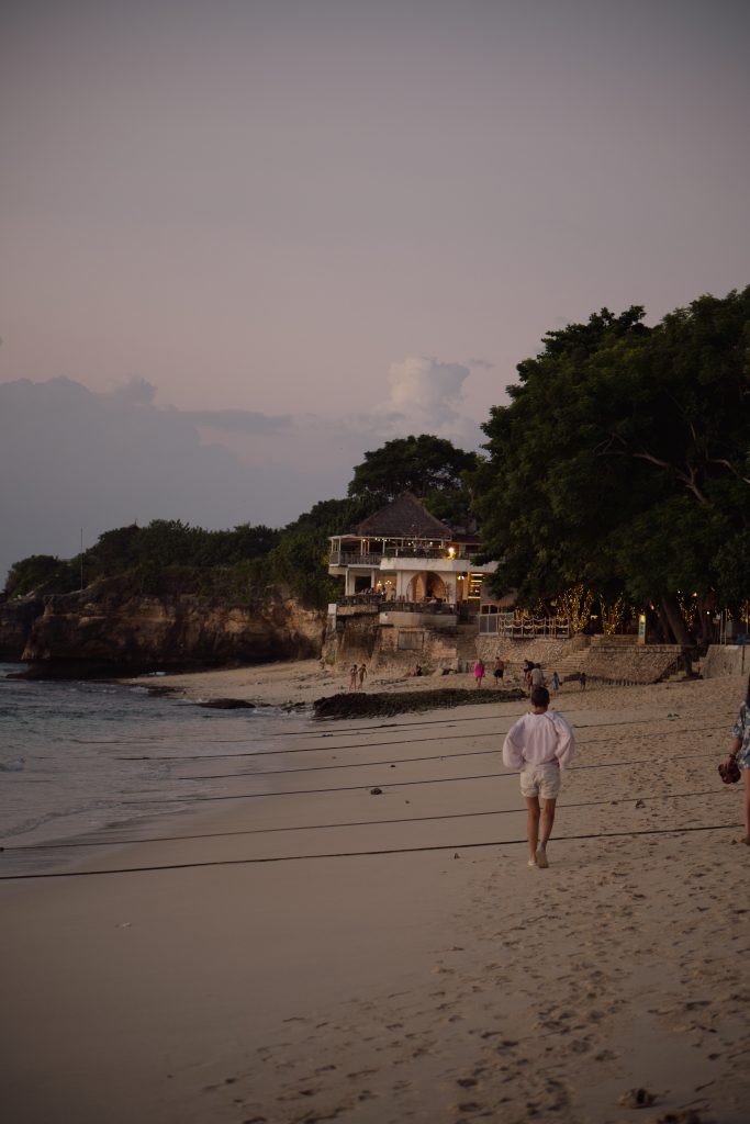 Person walking along the beach at dusk near a beachfront building on Nusa Lembongan