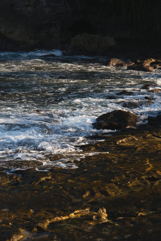 Waves crashing over dark volcanic rocks along Nusa Lembongan's shoreline