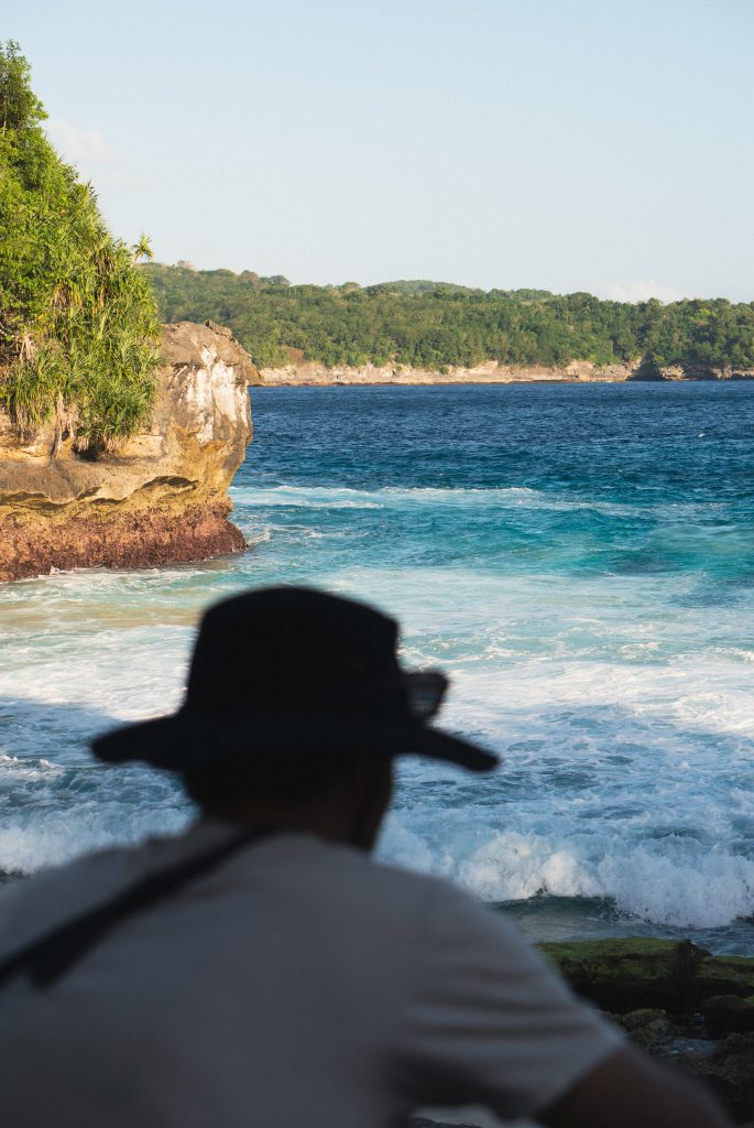 Traveler in a hat admiring the cliffs and turquoise sea at Secret Beach, Nusa Lembongan