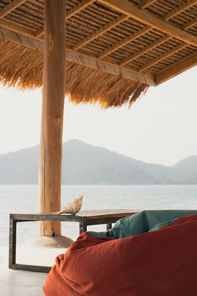 View of the sea and distant hills from a thatched open-air terrace with floor cushions in Sekotong