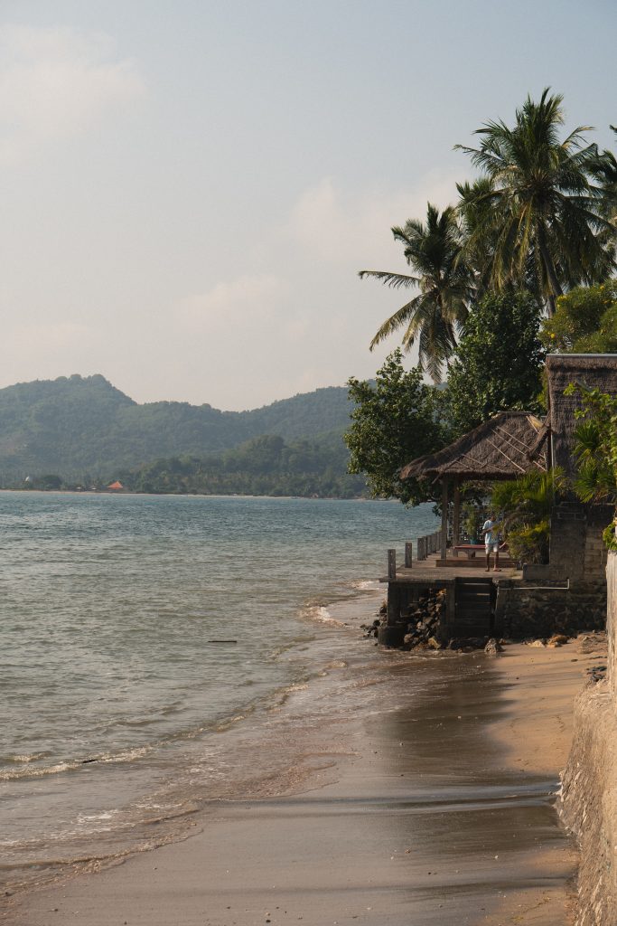 Calm shallow bay in Sekotong lined with palm trees and a small thatched pavilion at the water's edge