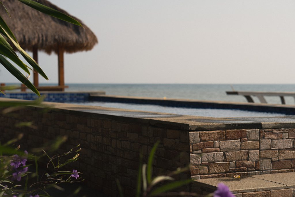 Hotel pool looking out to the sea, with a thatched gazebo and purple flowers in the foreground