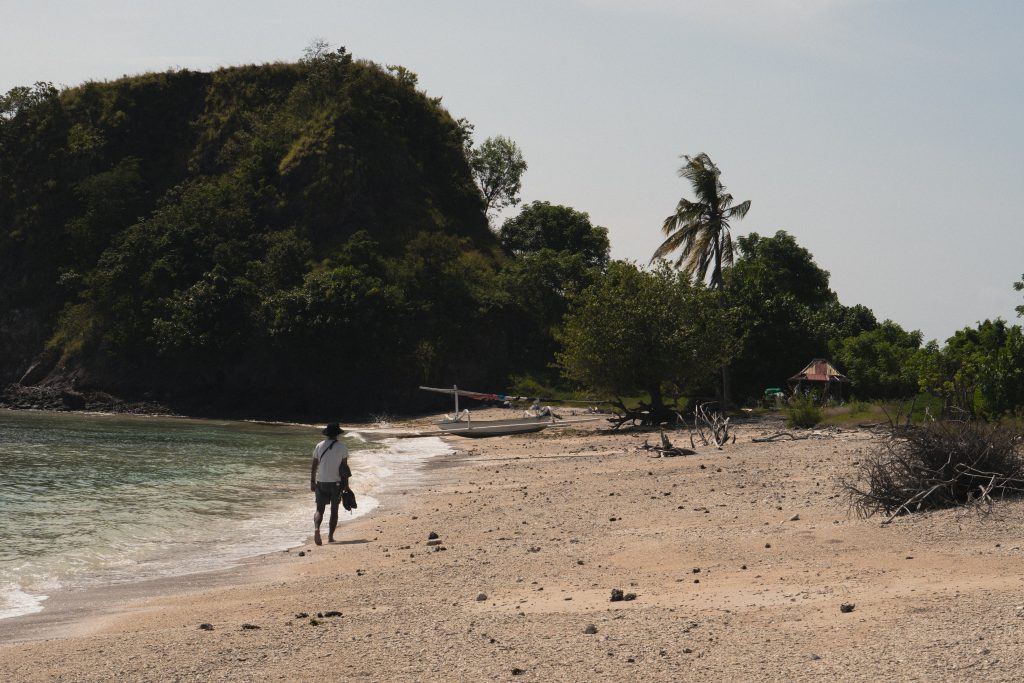 Person walking along the empty beach on Gili Asahan below a forested headland