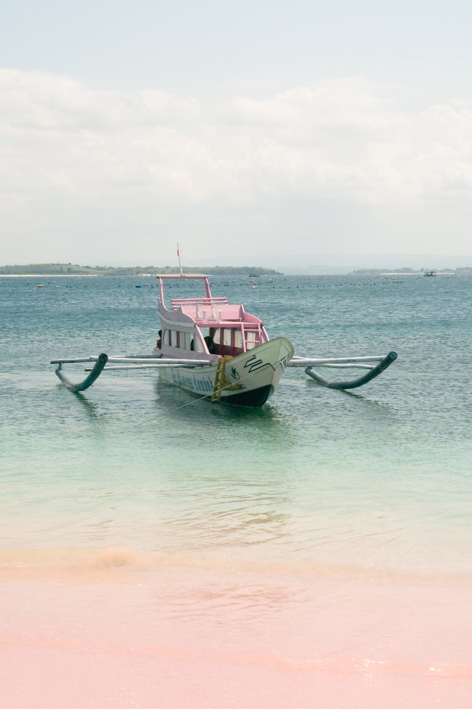 Traditional outrigger boat moored in shallow turquoise water at Pink Beach in East Lombok