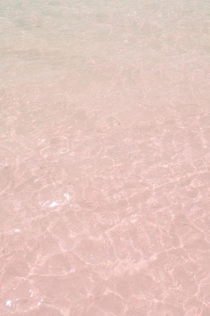 Close-up of the pink-tinted sand under clear shallow water at Pink Beach