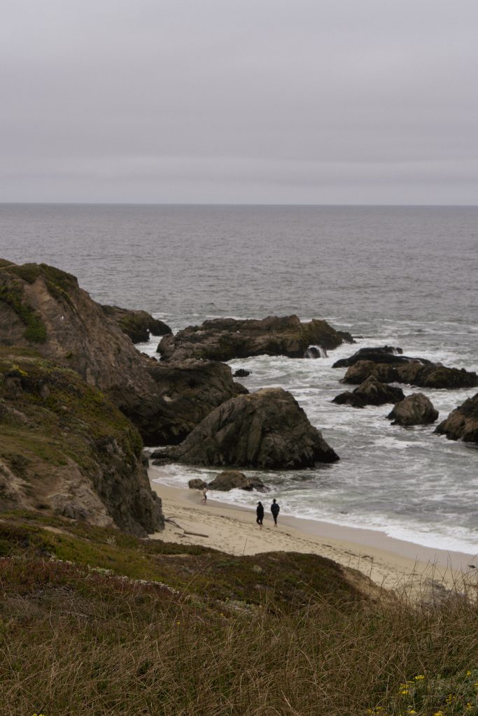 Two people walking on a small rocky beach on the Sonoma coast