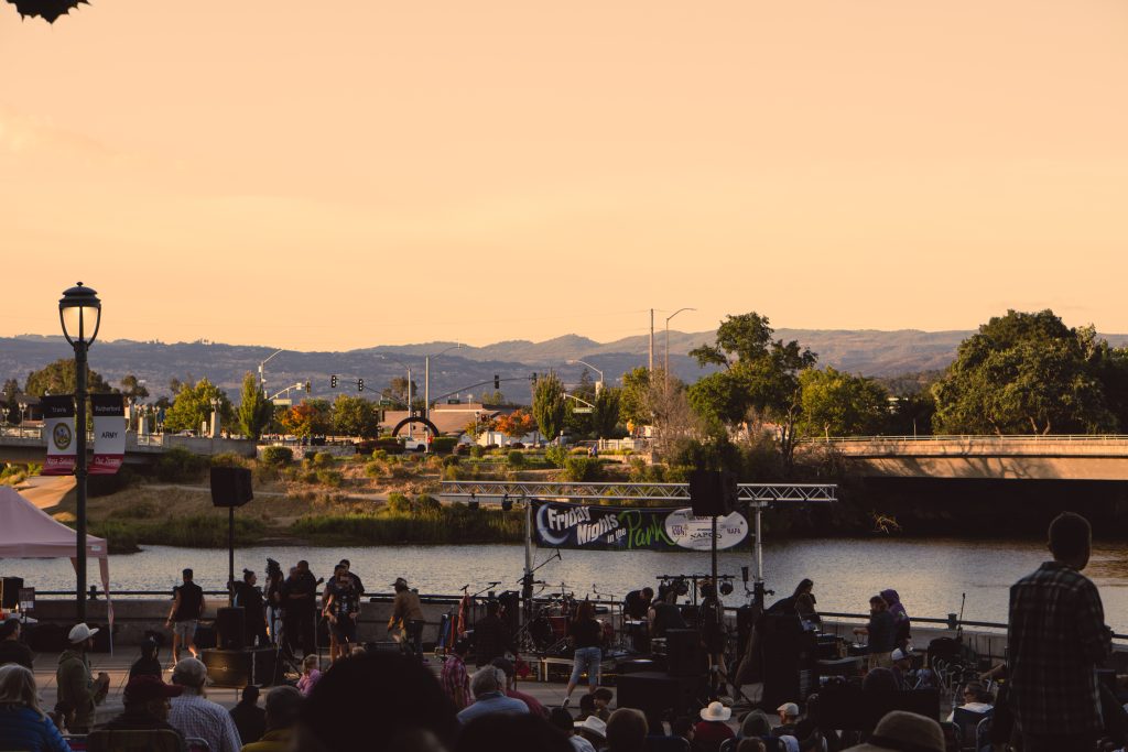 A crowd at a free outdoor concert beside the river in downtown Napa at sunset