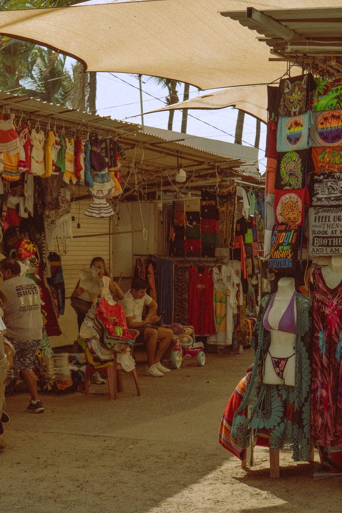 Beachwear and souvenir stalls under canvas shades at a street market in Puerto Vallarta's Zona Romantica