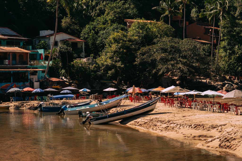 Wooden pangas pulled up on the sand at Playa Las Animas in front of colourful beachfront restaurants and umbrellas