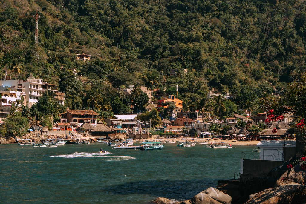 The village of Boca de Tomatlan seen from the water, houses stacked on a jungle hillside above the beach