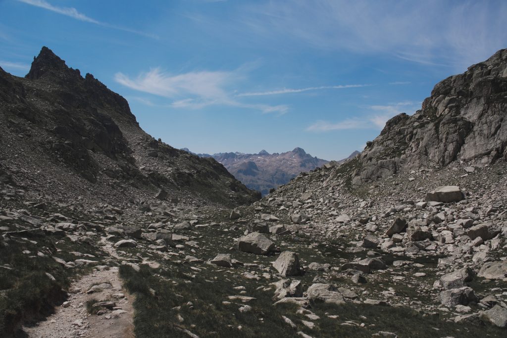 Rocky trail winding between rocky peaks under a blue sky, on the way to the Marcadau valley.