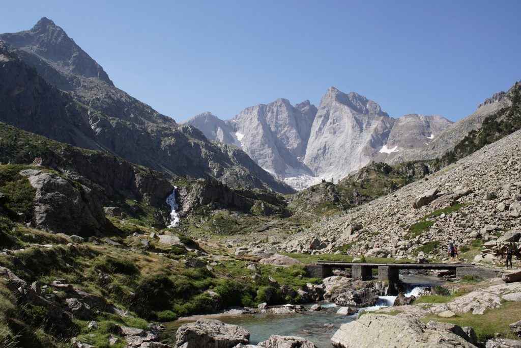 Rocky mountain valley with a stream and footbridge below a jagged peak