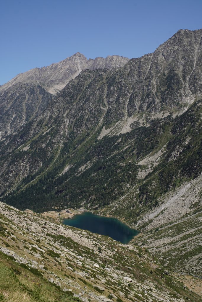 Aerial view of Lac d'Estom, a dark blue lake nestled in a rocky mountain basin