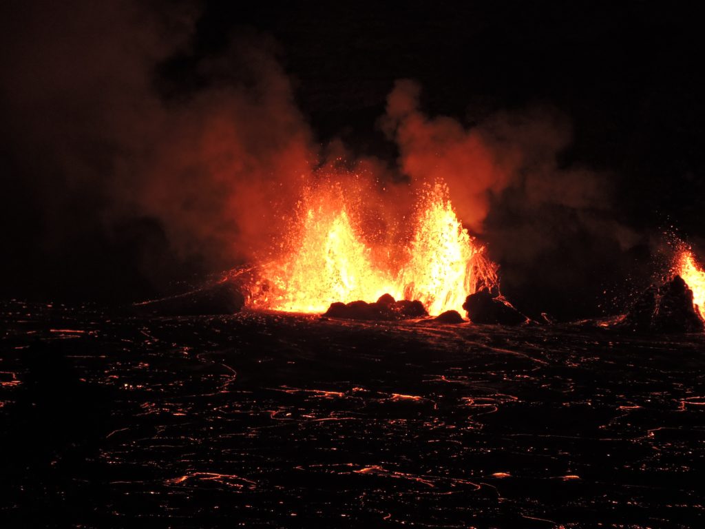 Lava fountains erupting from a vent at night, spraying molten rock across the crater floor