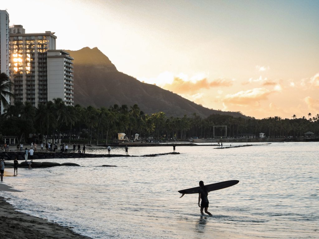 Surfer walking into the ocean at sunset in Waikiki with Diamond Head crater in the background oahu on a budget