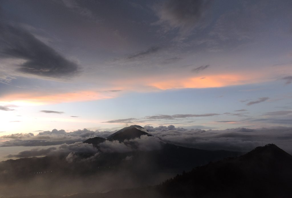 View from Mount Batur at dawn, clouds filling the caldera with volcanic peaks in the distance
