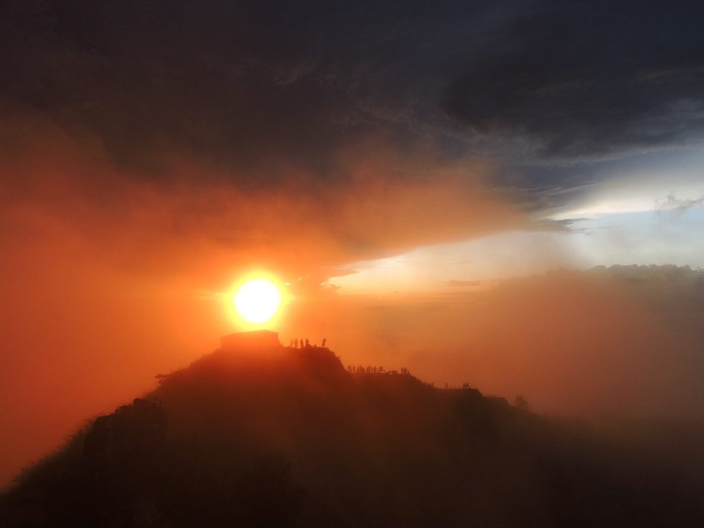 Sun rising over the ridge of Mount Batur with hikers silhouetted against an orange sky