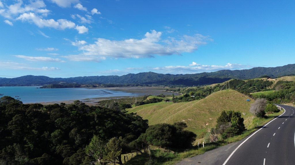 A winding coastal road on the Coromandel Peninsula with a curved bay and hills in the background