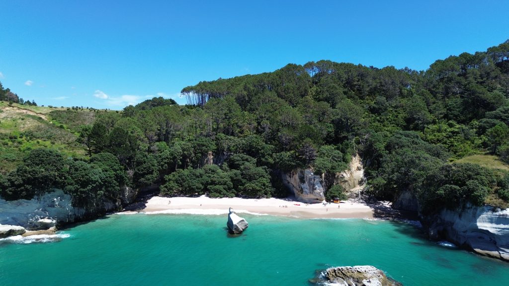 Aerial view of Cathedral Cove, Mautohe, showing the natural rock arch between two sandy beaches with turquoise water and Te Hoho Rock offshore