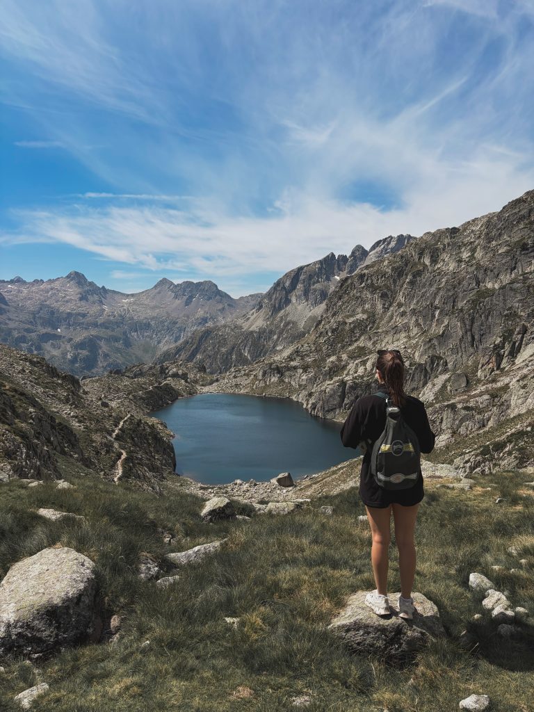 Randonneuse avec sac à dos admirant un lac de montagne depuis un promontoire rocheux.