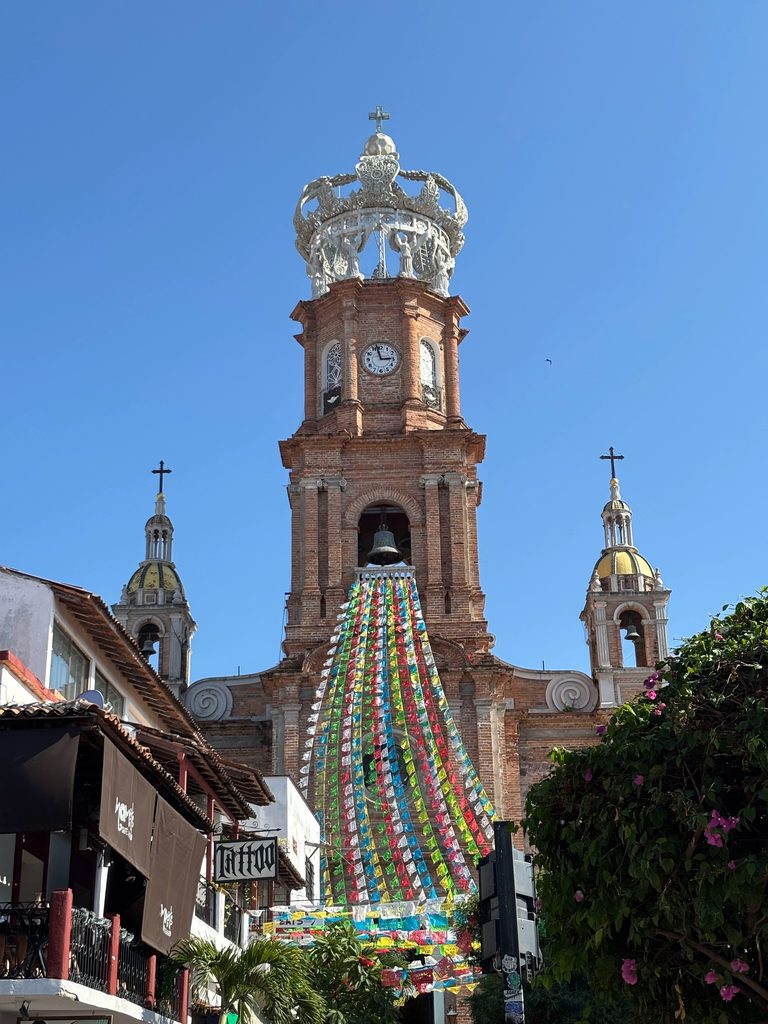 The crowned bell tower of the Church of Our Lady of Guadalupe in Puerto Vallarta, draped with papel picado garlands
