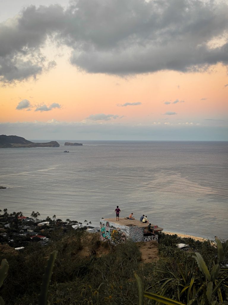 People sitting on a pillbox at Makapuu Point Lighthouse Trail watching the sunset over offshore islets