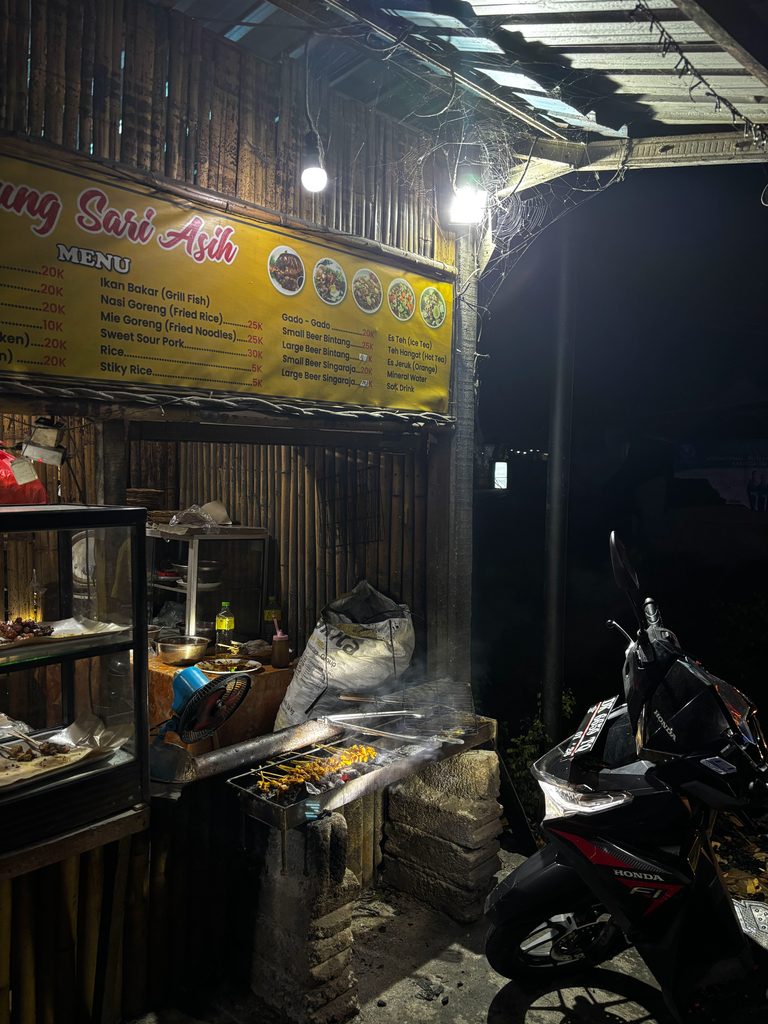 Skewers of tuna satay grilling over coals at Warung Sari Asih, a bamboo street food stall in Amed at night