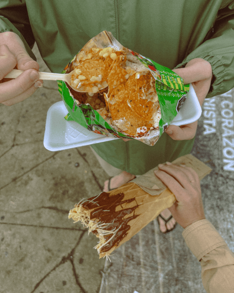 A freshly made marquesita topped with grated cheese, held in its paper wrapper at a street stand