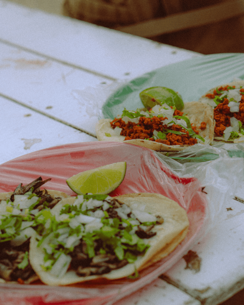 Close-up of tacos filled with a red-seasoned stew and topped with onion, coriander and lime