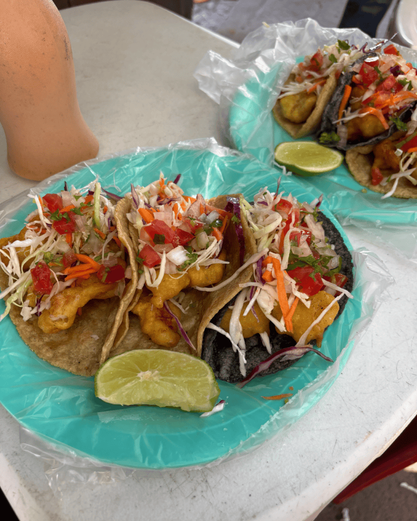Two paper plates of tacos topped with cabbage slaw, pico de gallo and a wedge of lime at a street food stall