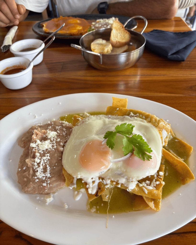 A plate of green chilaquiles topped with two fried eggs, crumbled cheese and fresh coriander