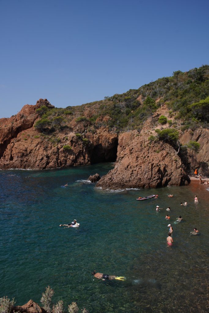 Small cove of red Esterel rock with swimmers in the clear turquoise water