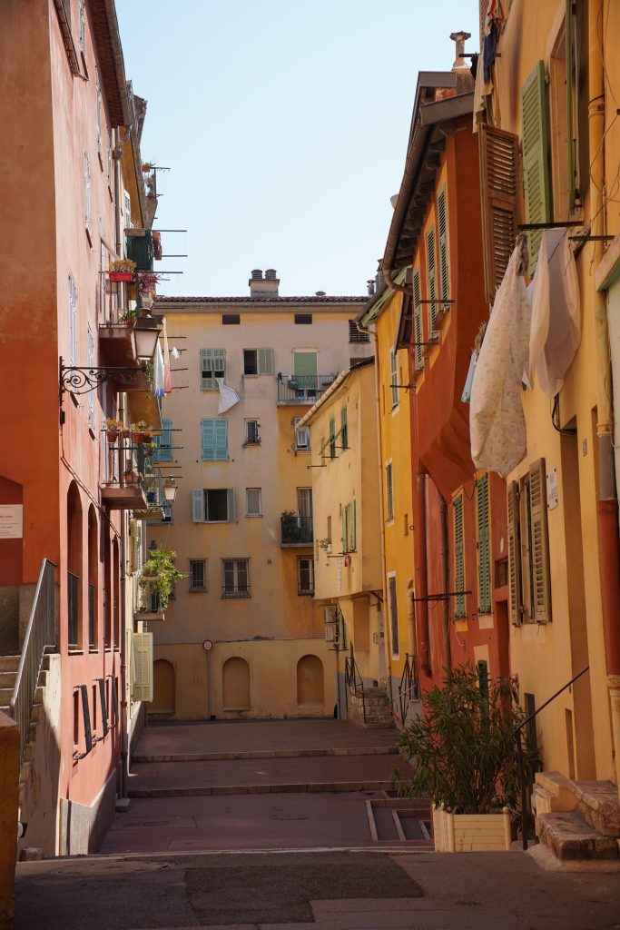 Sloping alley in Vieux Nice with pastel facades, green shutters and laundry hanging from the windows