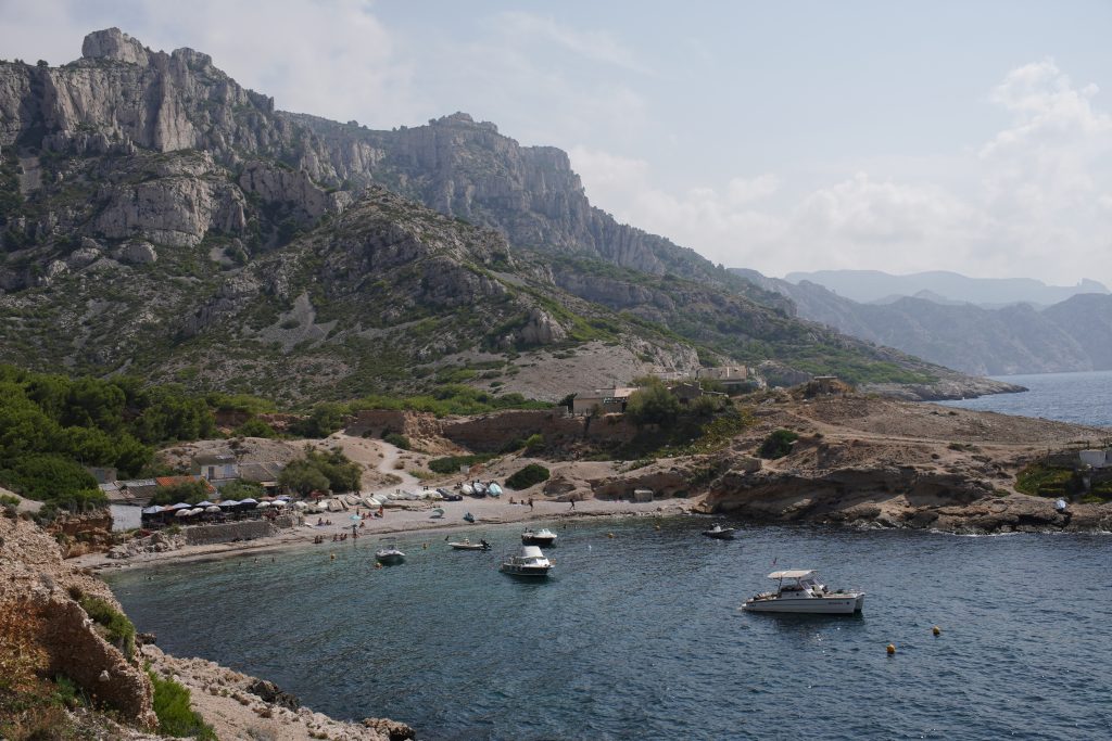 Rocky cove with moored boats and white limestone cliffs on the walk to the Calanque de Marseilleveyre