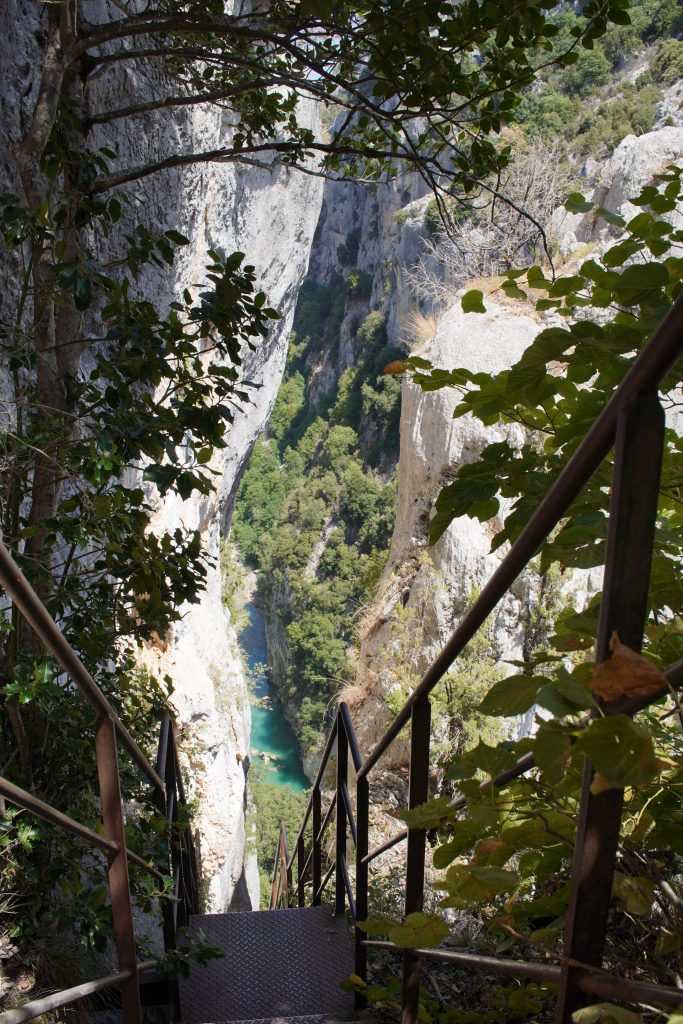 Metal staircase descending through greenery towards the turquoise Verdon river on the Sentier Blanc-Martel