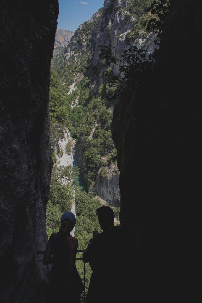 Two hikers silhouetted at the mouth of a rock tunnel on the Sentier Blanc-Martel in the Gorges du Verdon